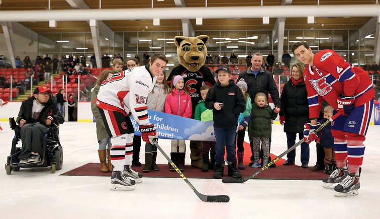 Jameson Jones drops the puck between Cariboo Cougars Riley Coish, and Vancouver North East Chiefs Marcus Murdock during a cermonial faceoff on Saturday at Kin 1. Jones was joined at centre ice by some former patients of the BC Children's Hospital and their parents, Rowdy Cat, and Shirley Bond, MLA for Prince George-Valemount. Citizen Photo by James Doyle January 9, 2016