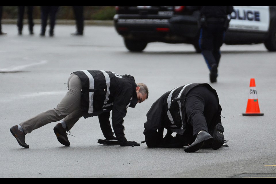 Independent Investigations Office investigators take a close look at a shell casing marked by a pylon in a Queensborough Landing parking lot, the scene of a police-involved shooting Friday.