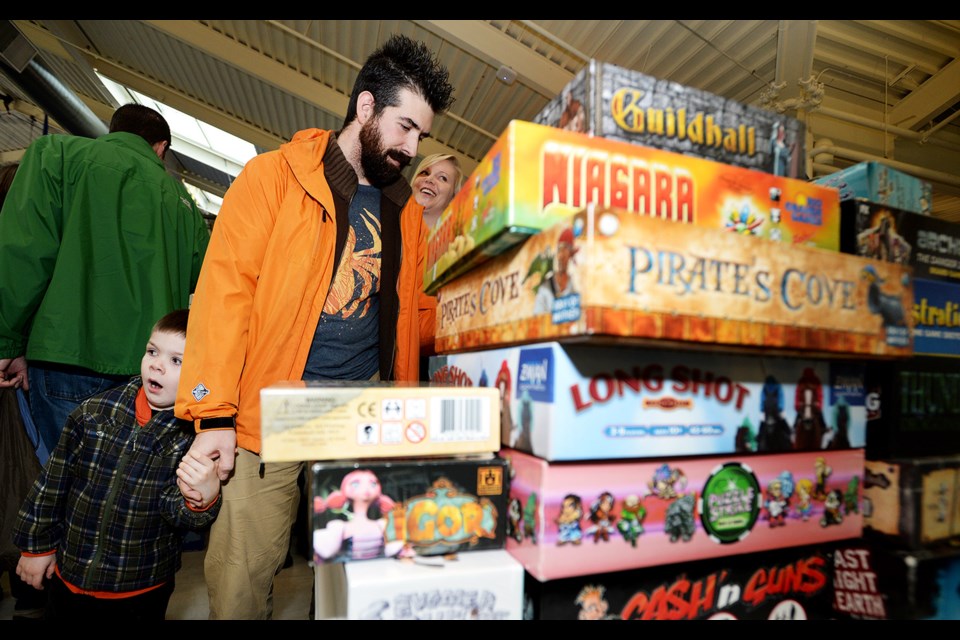 Six-year-old Benjamin might be a bit less than enthralled by the experience, but dad Jason Widdes looks interested in the offerings at a board game meetup and buy-sell-trade event Sunday at River Market.