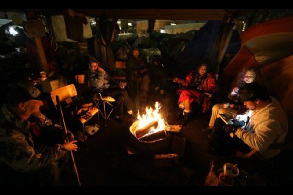 Tent city residents stay warm by the fire as night falls.
