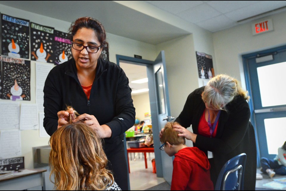 New Westminster parent volunteers Sukhi Plessis, left, and Gina Griffiths, right, check Lord Kelvin Elementary School students for lice and nits as part of a routine round of inspections after every major break.