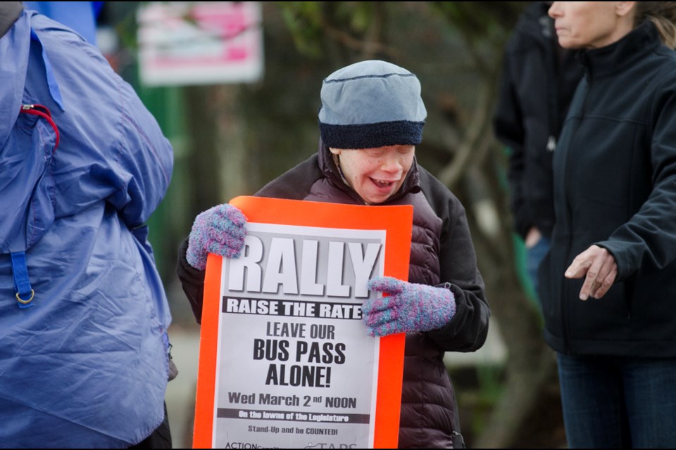 Melissa McCann holds a sign protesting changes to bus passes for people with disabilities during a rally at the Metrotown SkyTrain station Wednesday.