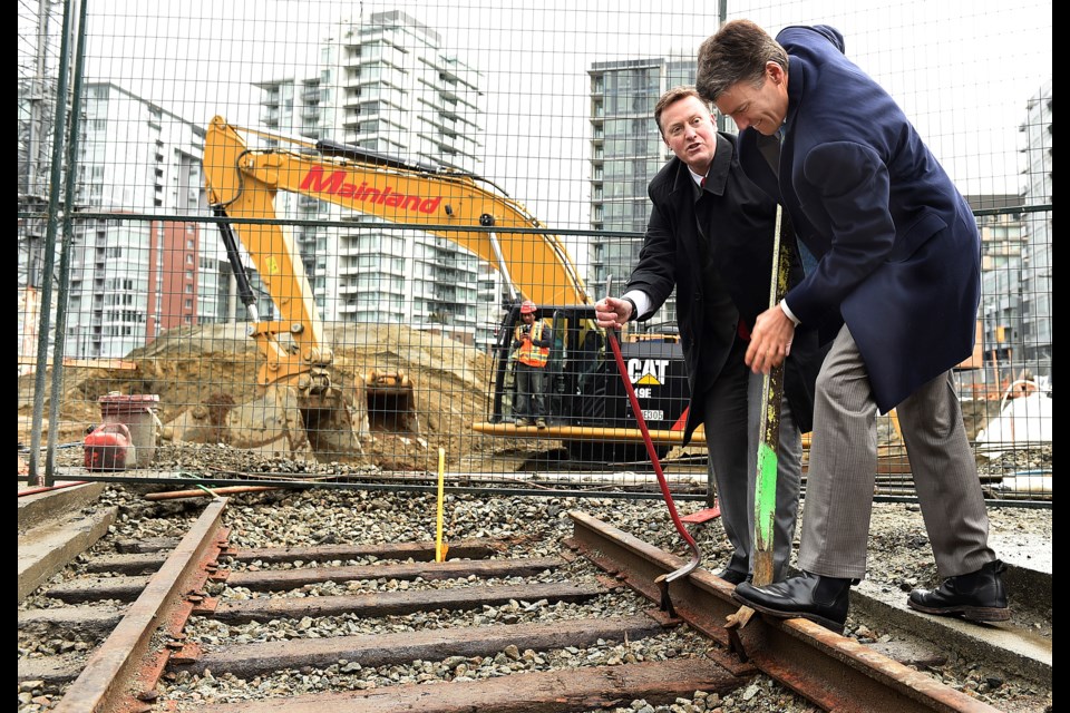 Brian McCauley, president and chief operating officer of Concert Properties, and Mayor Gregor Robertson participated in a photo opp Tuesday in which they removed spikes from a rail line on property slated for a five-building development that will include a rental tower. Photo Dan Toulgoet