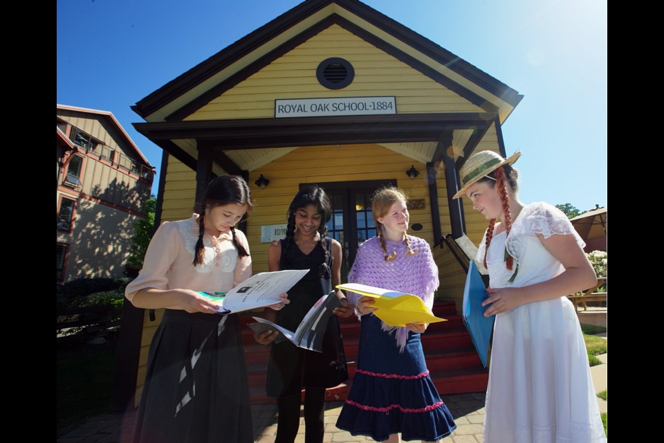 Royal Oak students, from left, Mina Choi, Samyukhta Prasath, Kate Spicer and Elena Mair celebrate the school's 150th anniversary in front of its oldest standing building, still used as a meeting hall. Wearing period costumes, the Grade 6 and 7 students hold social studies books they wrote on the school's history.