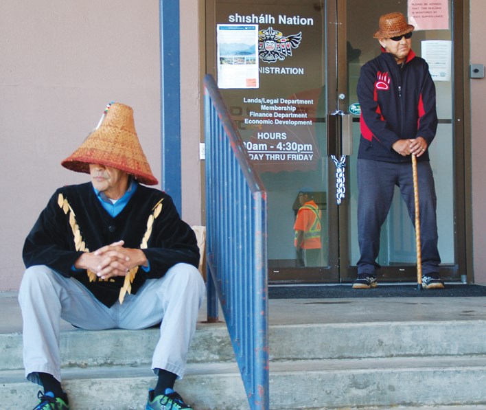 Chief Calvin Craigan sits on the steps of the shíshálh Nation administrative building Tuesday as band member Willard Joe stands guard over the locked entrance.