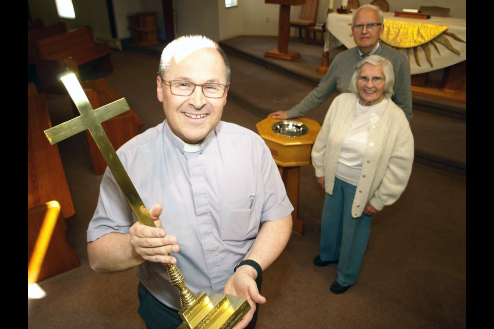 Rev. Brian Vickers, holding a cross dedicated to the founder of St. Anne’s church, and longtime members Mildred Hingston and Harold Shury are marking the parish’s 125th anniversary this year. Photo by Matthew Hoekstra/Special to the News
