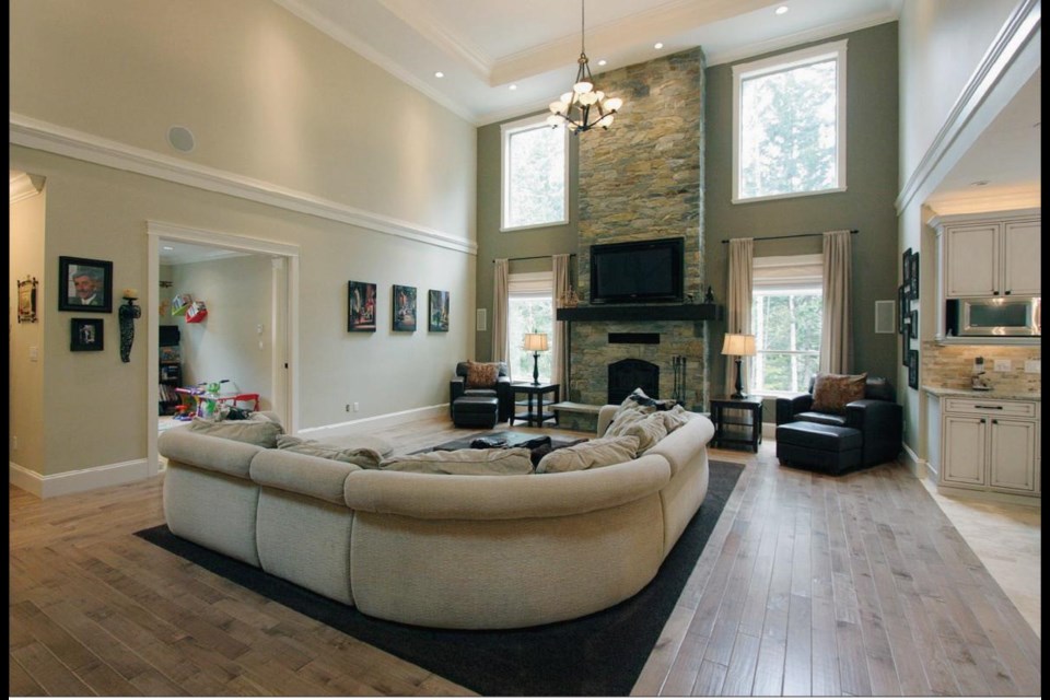 A massive stone fireplace and the heavy chandelier meld comfortably with the pillow-strewn sectional sofa and the modern kitchen.