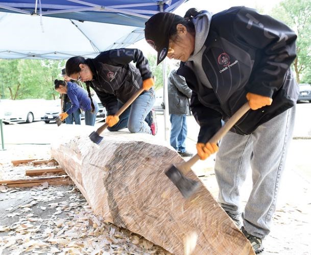 Volunteers carve the outside of a cottonwood dugout canoe on Monday at The Exploration Place. Once the canoe has made a voyage on the river it will be a part of an exhibit at The Exploration Place.