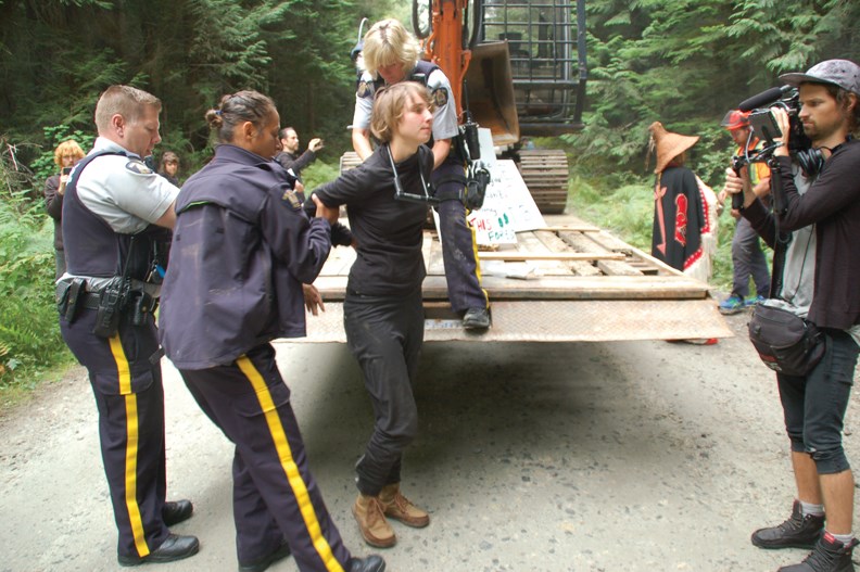 Sunshine Coast RCMP officers take a protester who gave her name as Salamander into custody on Sept. 9 after the young woman locked herself by the neck to an excavator with a bike lock in order to stop loggers from entering what some in the community have dubbed the Twist and Shout Forest on Mount Elphinstone. Officers were unable to cut off the lock and instead unhooked a hydraulic line to free the woman before taking her to jail for violating a court order by impeding logging in the area.