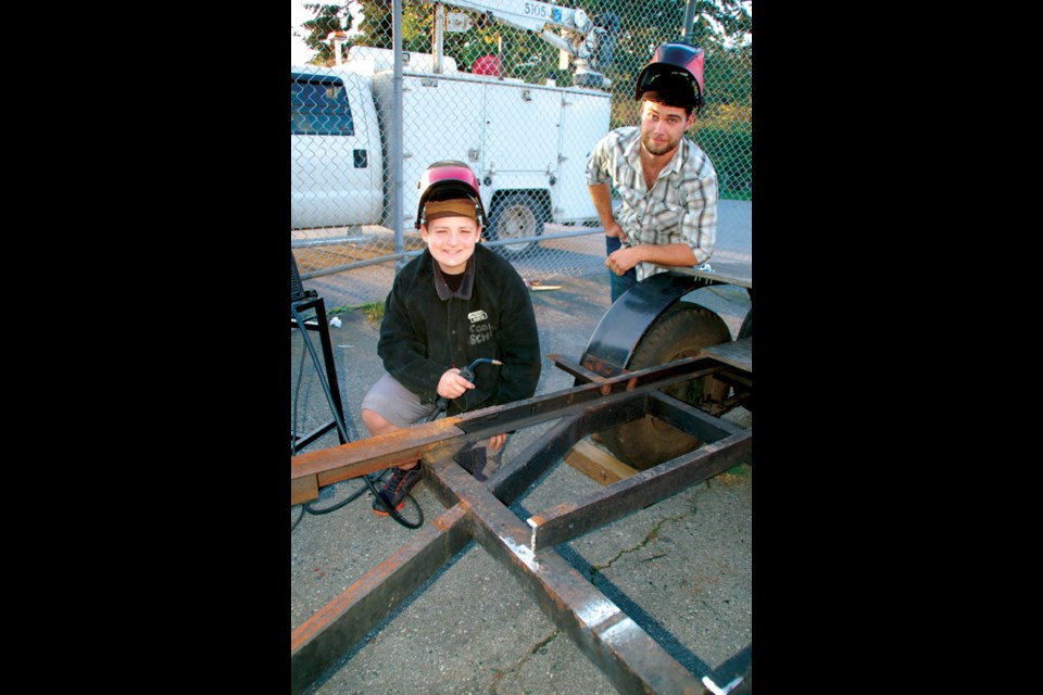 Cool School volunteer (and former student) Travis Hogson (right) helps student Vincent Hadjioannou with some welding on the trailer extension he’s creating that will haul the two dune buggies he plans to work on next at Cool School.
