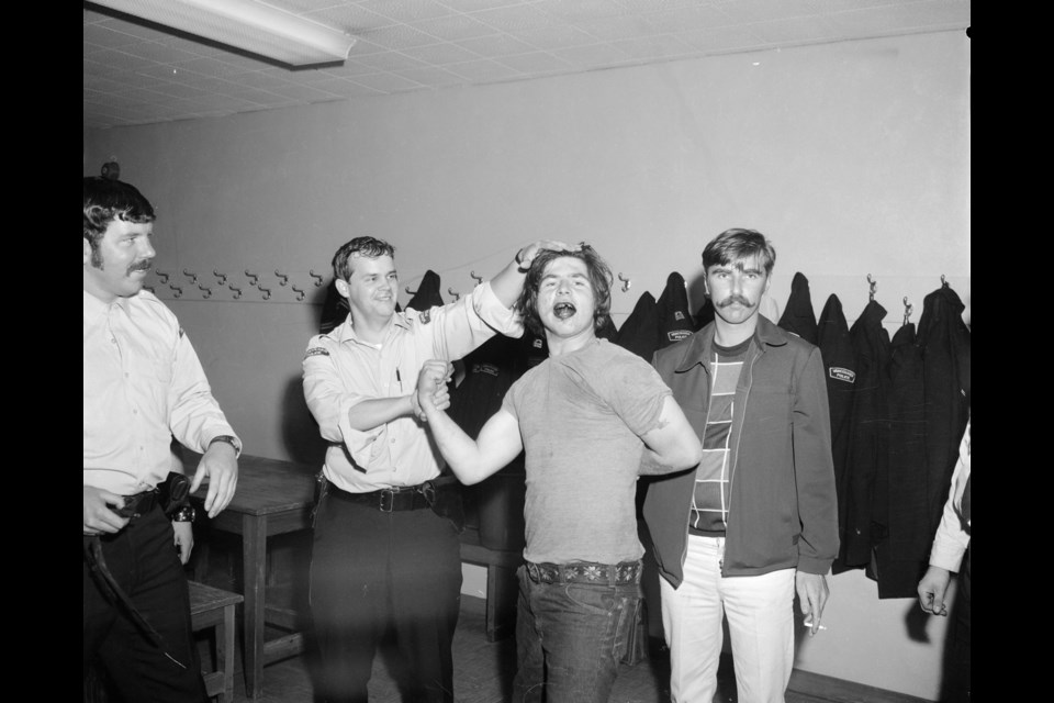 Constable Esko Kajander holds back Gerry Gavin for an arrest processing photo. Gavin smiles for the camera. Also pictured are Constable Stan Joplin (left) and Constable Mike Barnard (right). Photo Vancouver Police Museum, N005821