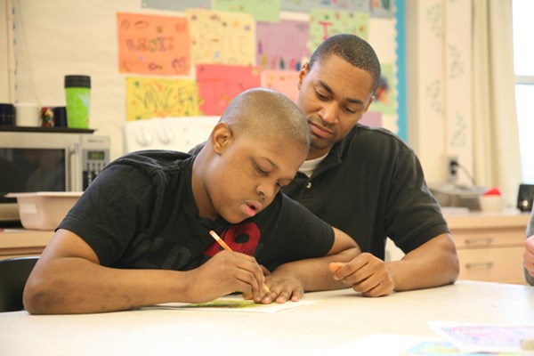 Student Support Worker Raymond Mitchell, who works in the Windermere Lifeskills class, helps Keith Martens draw a picture.