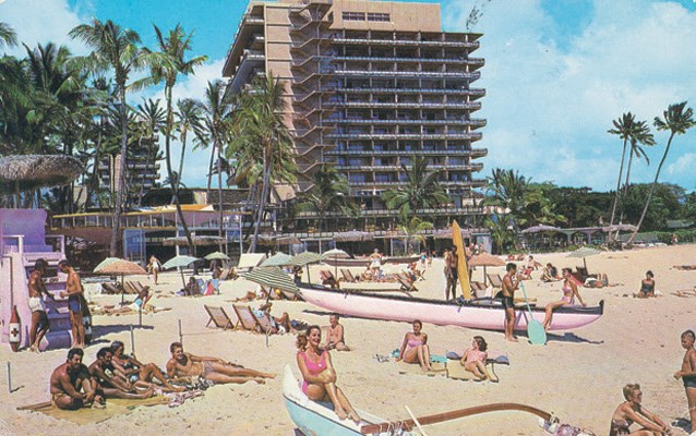 Sun worshipers and outrigger canoes outside the Hilton Hawaiian Village on Waikiki Beach in the 1960s.