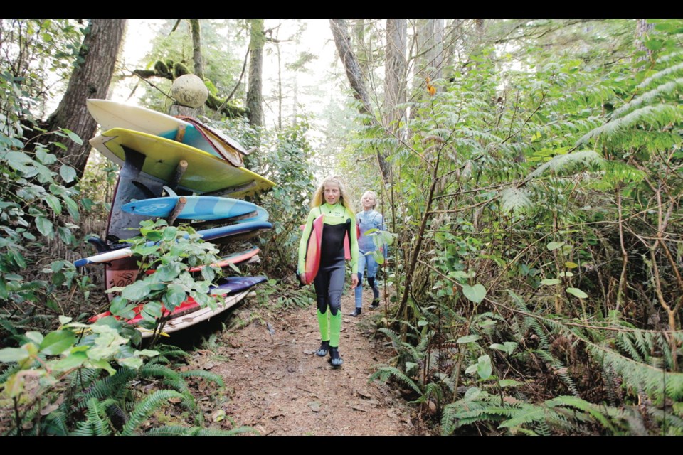 Sanoa Olin, 11, and her sister, Mathea Olin, 13, carry their surfboards along a path through their family's property, just a minute's walk from Cox Bay surf beach in Tofino.