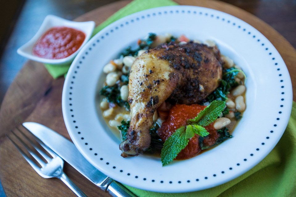 A Sunday dinner of succulent roasted chicken legs accompanied by cannellini beans with tomatoes and kale and harissa.