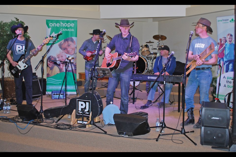 Prairie Joe warming up for their One Hope performance in Virden Alliance Church; (l-r) Thiessen brothers Michael on bass, Joe (back row l) electric guitar, Robert leading with accoustic guitar, Curtis Szakacs on keys (back row) and Russell on the washboard.