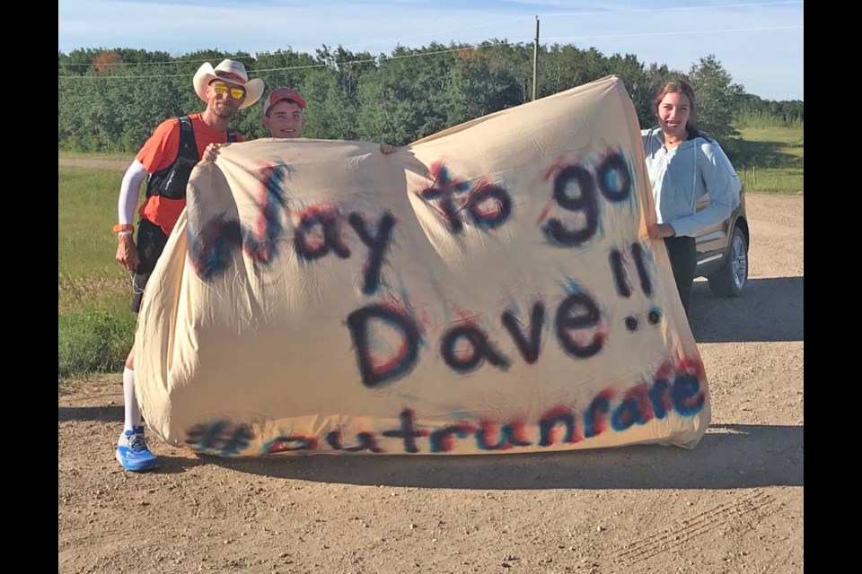 Cross Canada runner Dave Proctor (l) holding the welcome sign along with Cade (c) and Danika Scharff of Virden.
