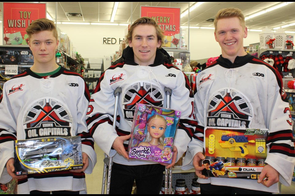 Oil Caps players (l-r) Riley Wallace, Parker Brakebill (on crutches due to game injury) and Dalton Dosch went shopping in Virden on Saturday, Dec. 8. They bought items at the Red Apple’s Fill-a-Sleigh Day for the local Christmas Cheer board. The event also featured Wallace District firefighters giving tours of their fire truck, volunteers carrying parcels out to cars, and Santa Claus greeting the kids.