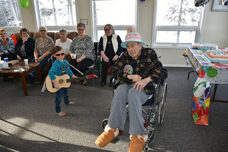 Ninety-nine-year old Ben Foord listens as his great-grandson strums Happy Birthday for him.