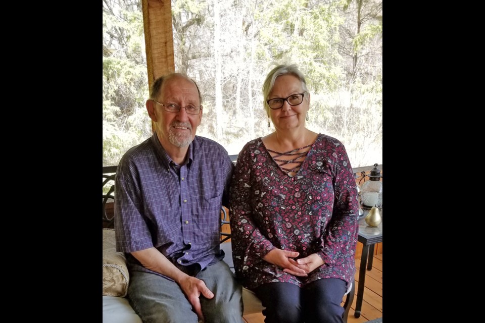 Uwe and Gail Jonas from Oak Lake's North Country sitting in their covered deck. The structure is supported by recycled telephone poles, run through Uwe’s sawmill; the electrically operated window coverings are his own invention as well.