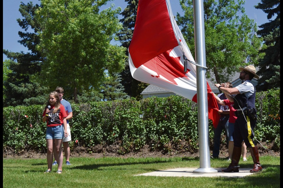 Young performer Charley Dunning of Virden sings O Canada as a super-sized flag is raised in Victoria Park Monday, July 1. The flag originally flew at the Peace Towers in Ottawa before being given to Virden veteran Jim Moffatt who later donated it to the Town of Virden. Raising the flag is Constable Paul Morissette of the Virden RCMP detachment.
