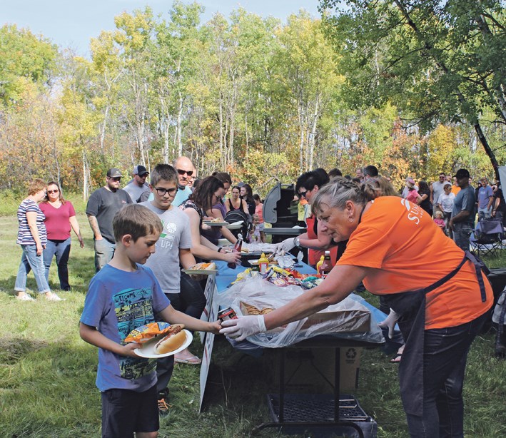 For the community barbecue, sponsors are hard at work serving lunch as a long line gathers on a record breaking hot and breezy Sept. 17. Monica Sweeting (Sunrise CU Ag Lender) serves Tydus Neufeld and his older brother Zeke (in background).