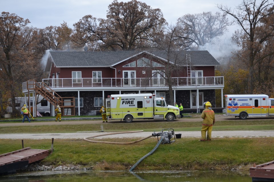 Fire department runs water hose from the Oak Lake marina to tackle tricky fire in upper level of large home on Marina Rd. on Monday morning.