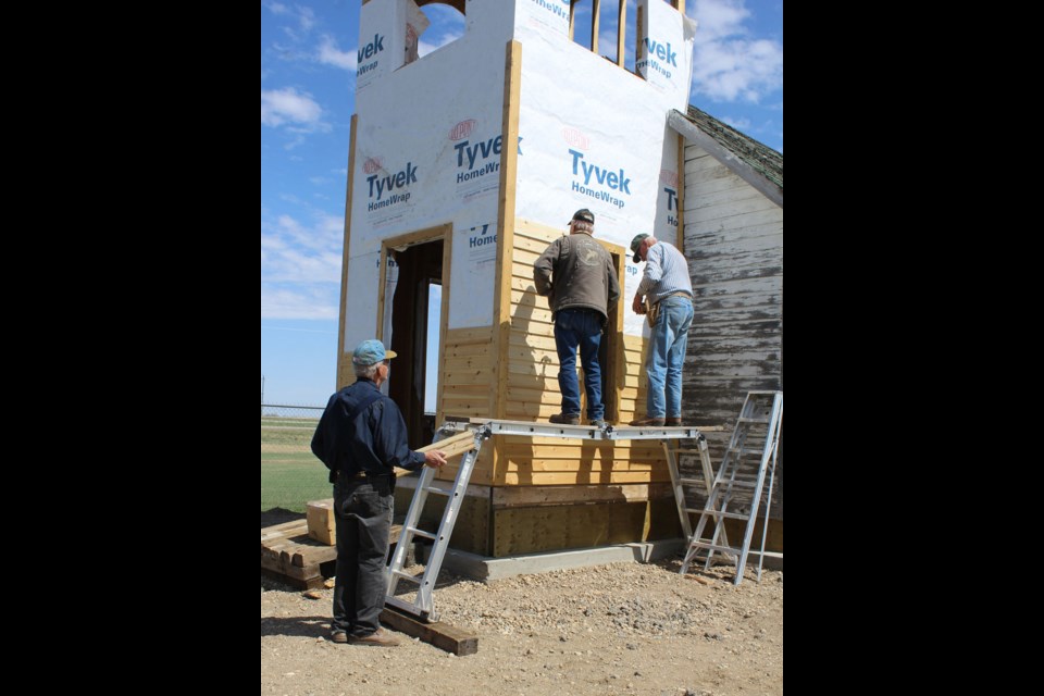 The Kirkella church at the new location, reconstruction of the bell tower in progress; (l-r) Lee Hodson, Herb Warkentin and his brother Sid Warkentin putting pine boards on the church bell tower.