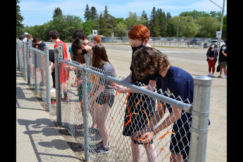 Students at Virden Collegiate Institute tie orange ribbons on the fence in front of the collegiate, in a memorium for the 215 bodies of children, discovered at Kamloops last week.