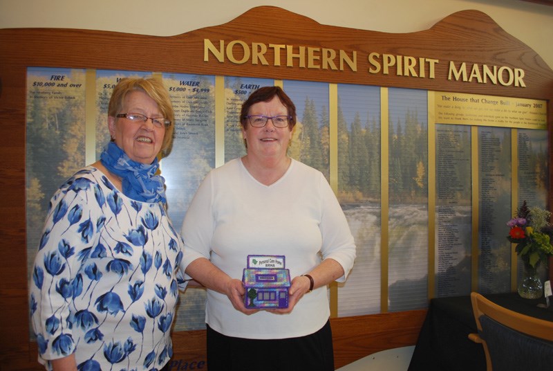 Sya Gregovski and Janet Brady, who were on the committee that raised over $400,000 to build Northern Spirit Manor, pose in front of the wall of donors during the 10th anniversary celebration.