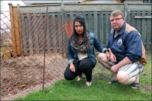 Deanna and Wayne Carriere kneel at a fence separating their yard from a section of land dug up