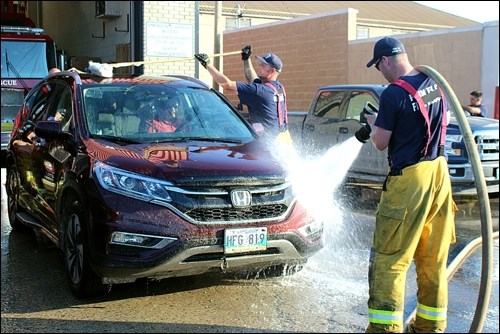 Firefighter Jon Smalley cleans off the roof of an SUV while Travis Ford takes care of the front bumper.