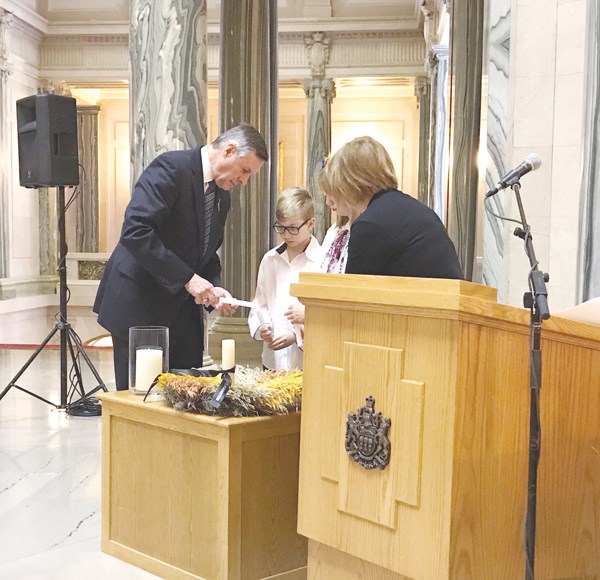 Minister Don Morgan and Mary-Anne Trischuk light a candle with Sophia Lazurko.