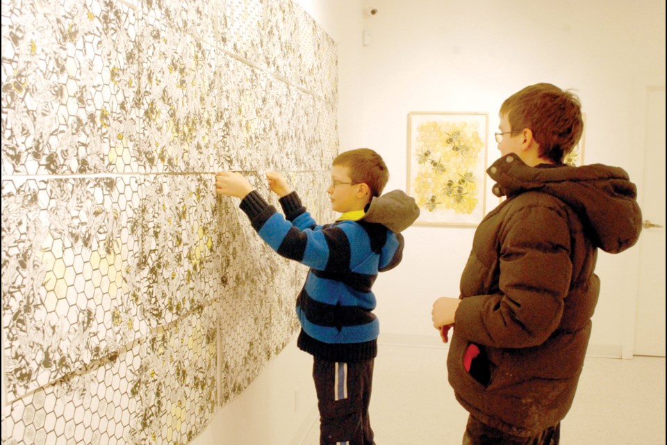 Monique Martin’s multisensory exhibit, Continuous, includes the sights and sounds of a beehive while also having an interactive wall where visitors to the Humboldt and District Gallery can make their own beehive. Visitors can choose between 250 panels to make the hive as healthy or unhealthy as they want. Pictured: Jordan and Kendel Reich work on their beehive during the Continuous opening reception on Jan. 10 at the gallery. photo by Becky Zimmer