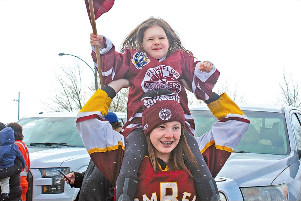 Tayler Krassilowsky flies a Flin Flon Bomber flag proudly on Anna Krassilowsky’s shoulders. The two, along with more than two hundred Bombers fans, came to cheer the team on March 22 as the Bombers’ bus left for Nipawin. The Bombers lost their game the next night, losing their playoff series 4-1 and ending their season.	- PHOTO BY ERIC WESTHAVER