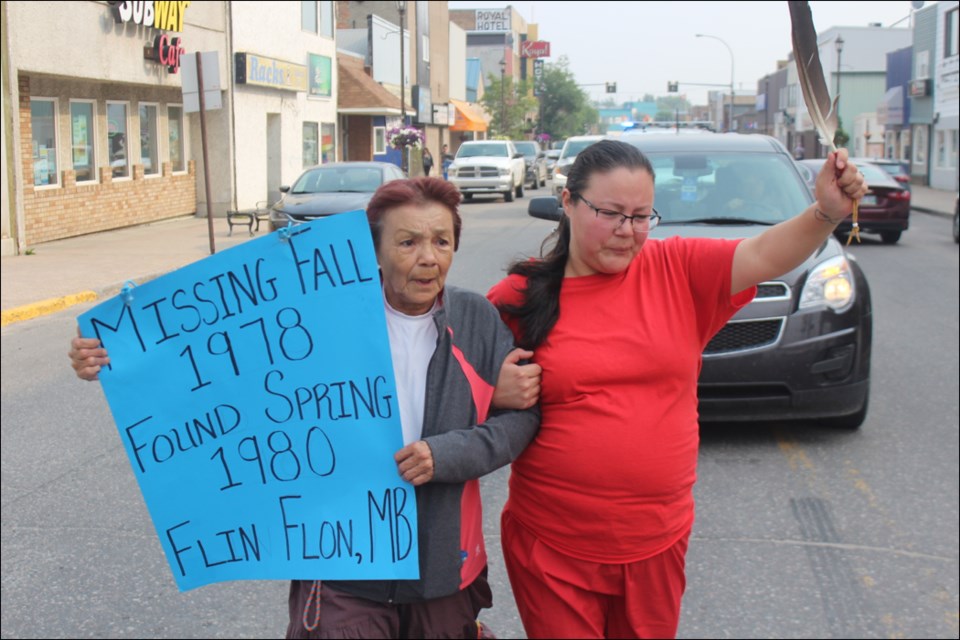 Margaret Doucette and Dionne Doucette march with a sign and an eagle feather at the memorial march for Flora Ballantyne on Aug. 18. Friends and family walked down Main Street to commemorate the life of Ballantyne, a Flin Flon woman who went missing and was found deceased in 1980. - PHOTO BY ERIC WESTHAVER