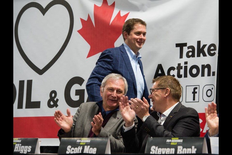 Andrew Scheer, centre, gets up to speak while New Brunswick Premier Blaine Higgs, left, and Saskatchewan Premier Scott Moe, right cheer him on.