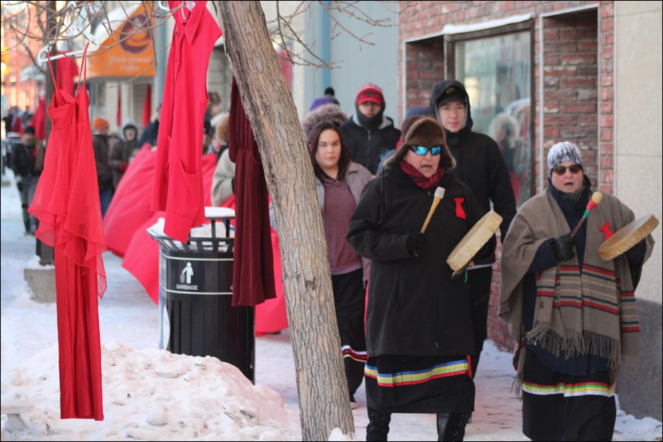 Cyndi O’Nabigon and Sylvie Dufour lead the way down Main Street past a skein of red dresses during the Women’s Memorial March Feb. 14. - PHOTO BY ERIC WESTHAVER