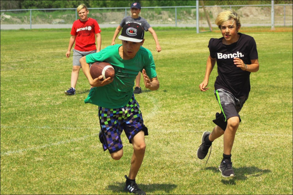 Creighton Community School student Evan Michel-McDermott runs the football while Owen Durette comes in to assist during a youth football session June 20 at the Creighton football field. - PHOTO BY ERIC WESTHAVER