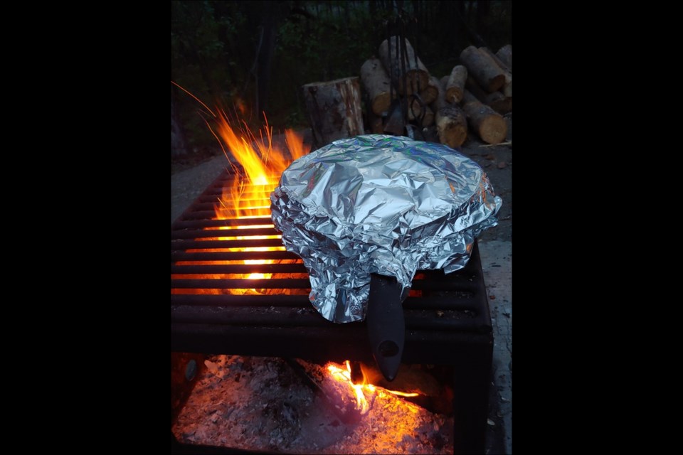 A plate of campfire nachos, wrapped in tin foil, sits cooking on the fire grate. - PHOTO BY TIM BABCOCK