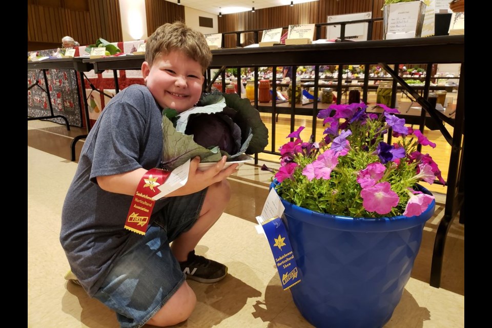 Grayson Dix, one of the five junior exhibitors, showed off his prizewinning potted plant, sporting a second-place ribbon, and head of cabbage exhibit which took first place in the junior fruit and vegetables category.