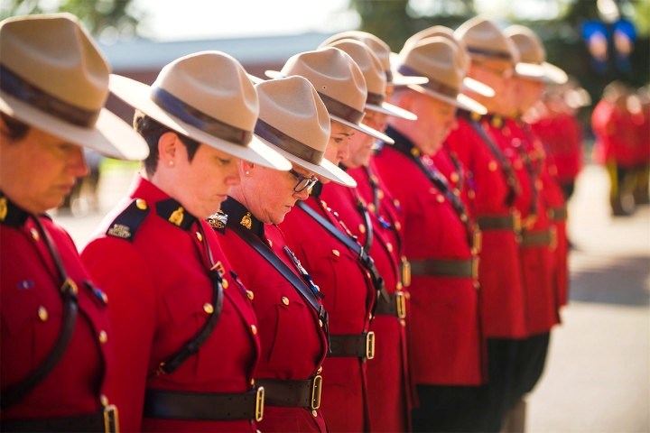 RCMP members in red serge bow their heads in remembrance.