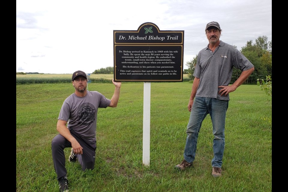 John Silvester, of Tsawwassen, B.C. and Barry Petruk of Togo stood by the dedication sign erected at the Kamsack disc golf course, dedicated to the Dr. Michael Bishop Trail, a community built walking trail adjacent to the disc golf course. Hole 6 is directly behind Silvester’s left shoulder.