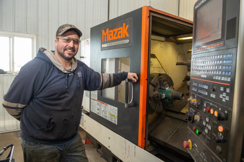 The specialized, automated pipe rack behind Nick Bourassa aligns and then inserts pipe into a porthole in the wall, allowing it to be worked on by a CNC lathe inside. Photo by Brian Zinchuk