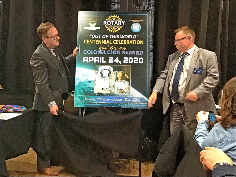 Ben Christensen and Warren Williams unveil the poster for Rotary’s “Out of This World” Celebration with keynote speaker Chris Hadfield, set for April 24, 2020. Photo by John Cairns