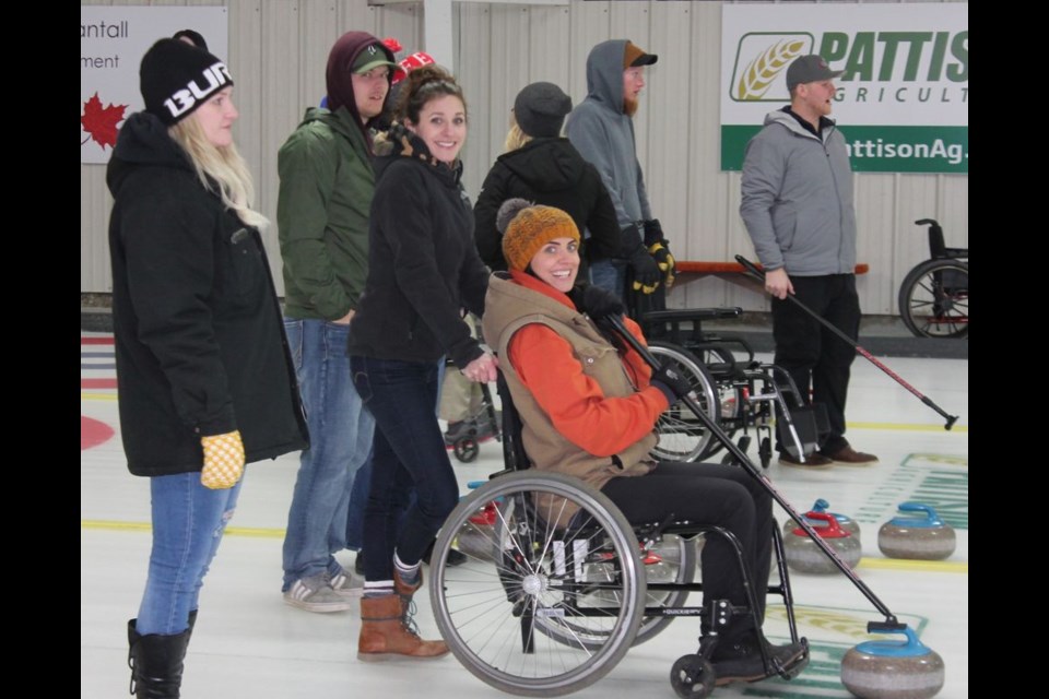 Jenna Bowes, seated, prepared to send a rock down the ice while Jodi Sas steadied the wheelchair, and Amanda Vidomski looked on during the Wheelchair Funspiel Fundraiser at the Broda Sportsplex.