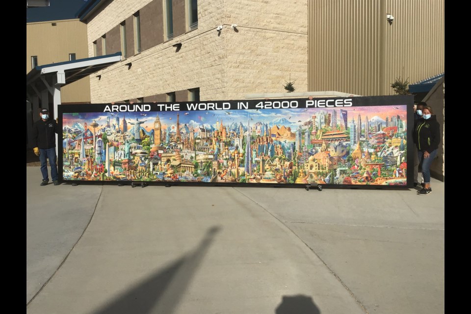 Cutline: Victor and Elaine Liebaert hold up the Around the World puzzle, the “world’s largest puzzle in a single image. The project took them almost two years to put together and was delivered to Saskatchewan Hospital Wednesday.