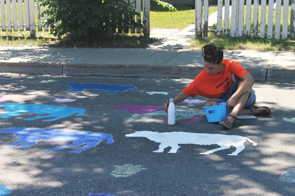 Savannah Kosteniuk is painting on one of the chalk murals designed by artists on Dewdney Avenue, which were open to help from the public throughout the day.