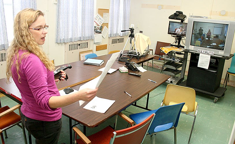 Mary Deren explains how the Telehealth video-conferencing equipment works, in its small conference room on the second floor of the Weyburn General Hospital, as she highlights the need for a new hospital facility. The Telehealth videoconferencing technology is invaluable for use in providing staff and public education on health issues, but also to hook doctors or patients up with doctors and specialists in other locations; for educational conferences, however, this small space is very inadequate. The only other space available is a conference room in the basement of the hospital, where pipes labelled "asbestos" are hooked into the radiators along the wall, and the room is only slightly larger than this one.