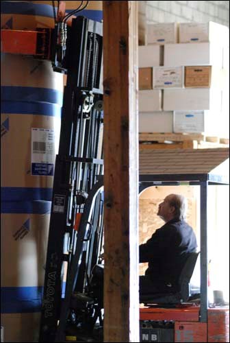 Rolls of paper weighing nearly one thousand pounds are unloaded from a trailer and stacked in the warehouse.e.